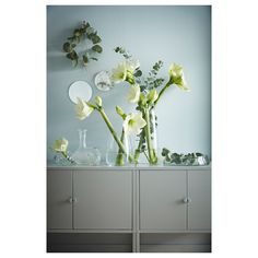 flowers in vases on top of a cabinet against a blue wall with mirrors above it