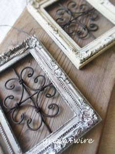 two ornate metal frames sitting on top of a wooden table next to an old window