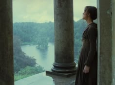 a woman standing in an open doorway looking out at the water and hills behind her