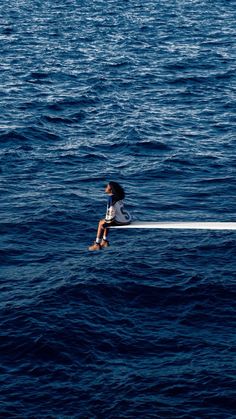 a woman sitting on top of a boat in the middle of the ocean with her back to the camera