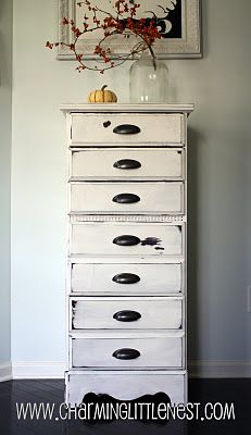 a white dresser with black drawers and an orange flower in a glass vase on top