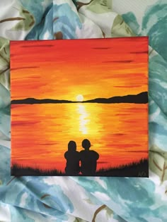 two people sitting on the edge of a body of water with an orange sunset in the background