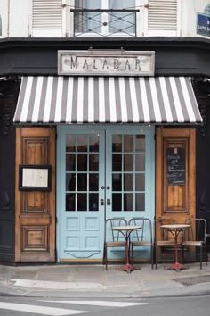 two tables and chairs are in front of a blue door with striped awnings