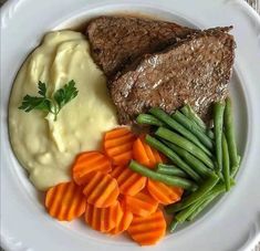 a white plate topped with meat, mashed potatoes and green beans next to carrots