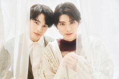 two young men standing next to each other in front of a white curtain and wearing sweaters