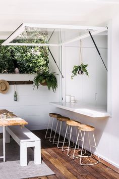 a table and some stools in a room with plants on the wall behind it