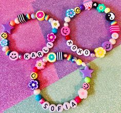 two colorful bracelets with name beads and smiley faces on them sitting on a purple background