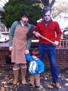 two adults and a child standing in front of a brick wall with leaves on the ground