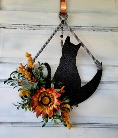 a black cat hanging on the side of a building with flowers in front of it