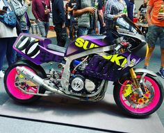 a purple and black motorcycle parked on top of a gray floor next to other people