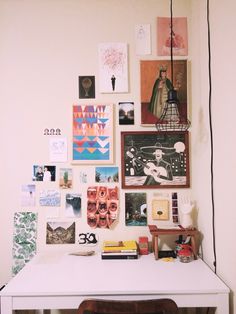 a white desk topped with lots of pictures and art on it's wall next to a brown chair