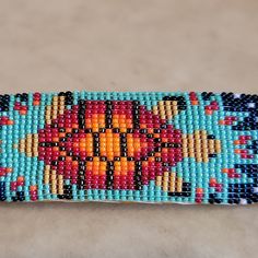 a beaded bracelet with an orange and blue design on the front, sitting on a table