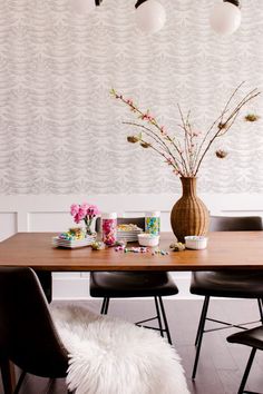 a wooden table topped with black chairs next to a vase filled with pink and white flowers