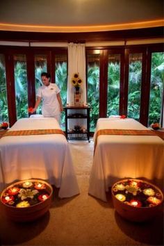 two massage tables with candles on them in front of large windows and a man standing next to each other