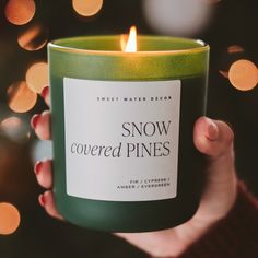 a person holding a candle in their hand with the words snow covered pines on it