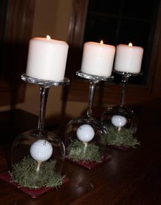 three wine glasses with golf balls in them sitting on a table next to two candles