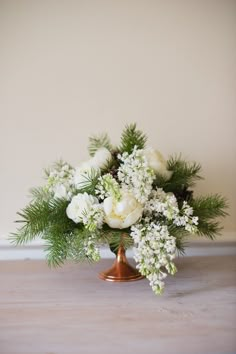 a bouquet of white flowers and greenery in a copper vase on a wooden table