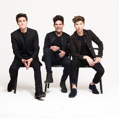 three young men sitting next to each other on top of a wooden bench in front of a white background