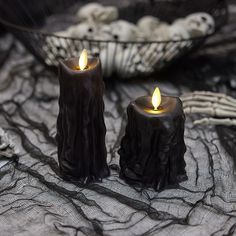 two black candles sitting on top of a table next to skeleton hands and skulls in the background