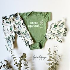 a baby's bodysuit, pants and headband are laid out next to plants