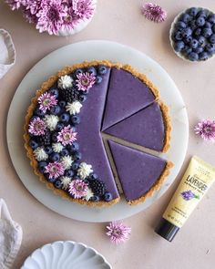 a blueberry cheesecake on a plate next to flowers and a tube of cream