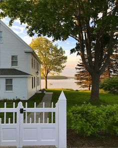 a white picket fence in front of a house with trees and water in the background