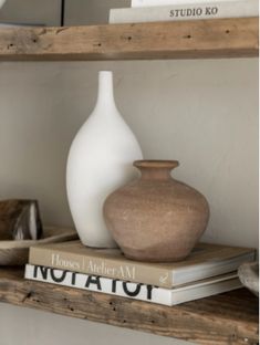 two white vases sitting on top of books in a shelf next to each other