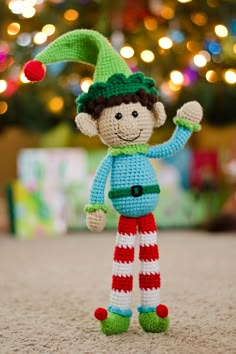 a crocheted elf doll standing in front of a christmas tree