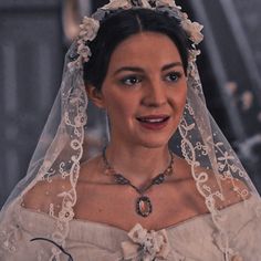 a woman in a wedding dress with a veil and flowers on her head is smiling at the camera