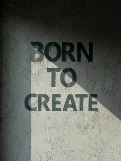 the words born to create are projected on a concrete wall with shadow from a window