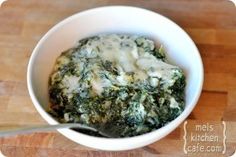 a white bowl filled with spinach and cheese on top of a wooden cutting board