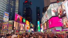 a crowd of people standing in the middle of a busy city street at night time