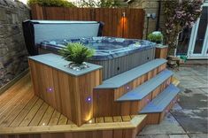 a hot tub sitting on top of a wooden deck next to a stone wall and planter