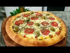 a pizza with tomatoes, olives and cheese on a wooden platter sitting on a kitchen counter