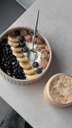 a bowl filled with cereal, bananas and blueberries next to a cup of coffee