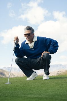 a man kneeling down on top of a lush green field holding a golf club in his hand