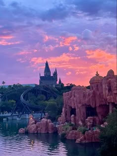 an amusement park with a roller coaster in the background at sunset or sunrise, as seen from across the lake