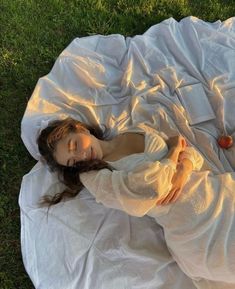 a woman laying on top of a white blanket in the grass next to an apple