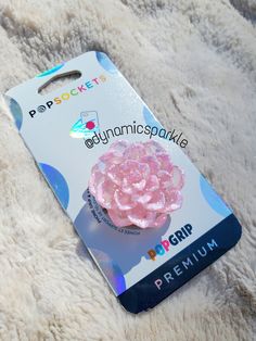 a phone case with a pink flower on it sitting on a white fur covered surface