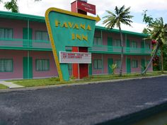 a motel sign in front of a pink and green building with palm trees around it