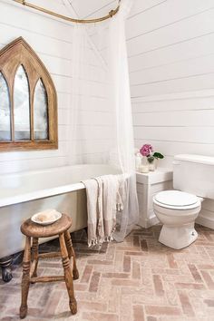 a white toilet sitting next to a bath tub in a bathroom under a stained glass window