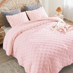 a bed with pink comforter and pillows on top of it, next to a lamp