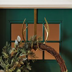 a wreath with antlers hanging from it's side next to a green door