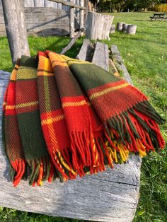 an orange and green plaid blanket sitting on top of a wooden bench in the grass