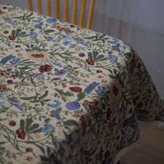 a table with a flowered cloth on it next to a wooden chair and window