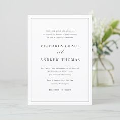 a white wedding card with the words victoria grace and andrew thomas on it, sitting next to a vase filled with flowers