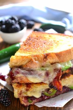 a grilled cheese sandwich with blackberries and green beans on a cutting board next to a bowl of berries