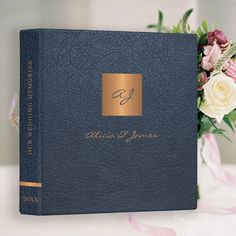 a blue book with gold foil on the cover next to a bouquet of white and pink flowers