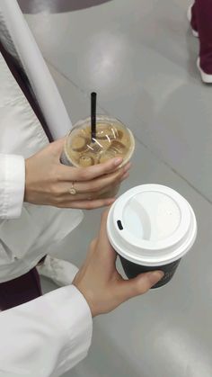 a person holding a coffee cup with a lid and straw in one hand, while another holds a paper cup with a lid on the other