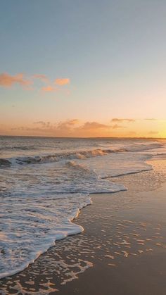 the sun is setting over the ocean with waves coming in